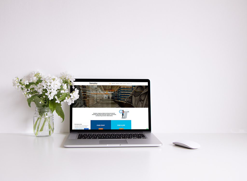 A laptop displaying the bemplay website, featuring a clean design with a focus on workforce solutions, sits on a minimalist desk alongside a vase of white flowers, showcasing a modern workspace aesthetic.